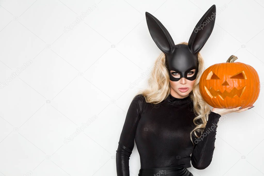 Beautiful young woman in halloween bunny costume, standing beside easter basket and holding pumpkin
