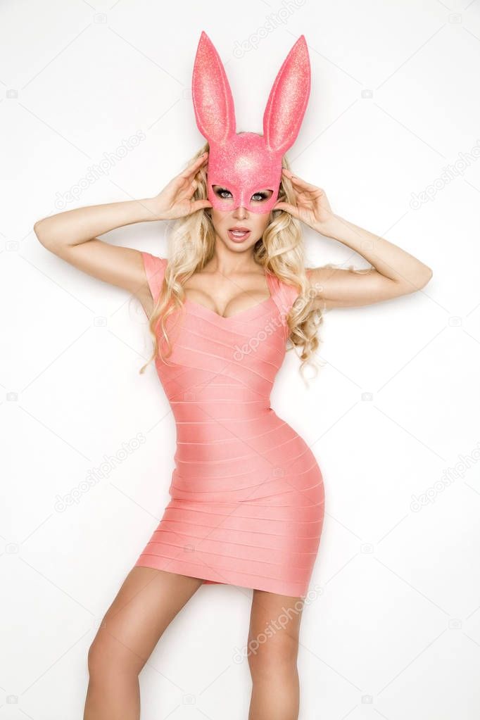 Beautiful sexy, young woman in halloween pink costume and pink mask, standing on white background