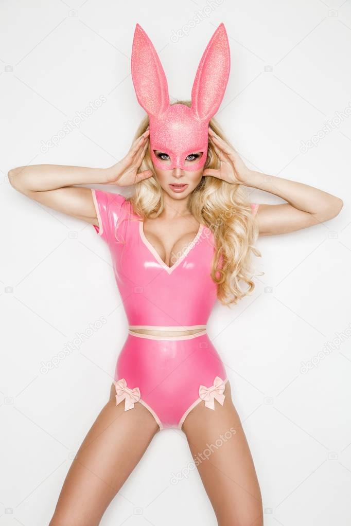 Beautiful sexy, young woman in halloween pink costume and pink mask, standing on white background