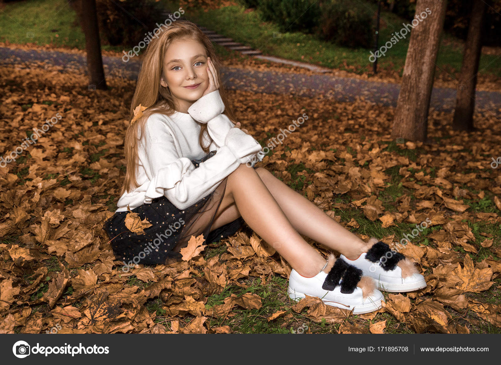 Cute little girl dressed in coat and boots sitting on autumn background ...
