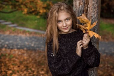 Sevimli küçük kız ceket giymiş ve çizmeler, sonbahar arka plan üzerinde oturan altın sonbahar yaprakları.