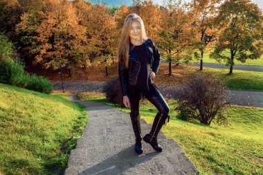 Sevimli küçük kız ceket giymiş ve çizmeler, sonbahar arka plan üzerinde oturan altın sonbahar yaprakları.