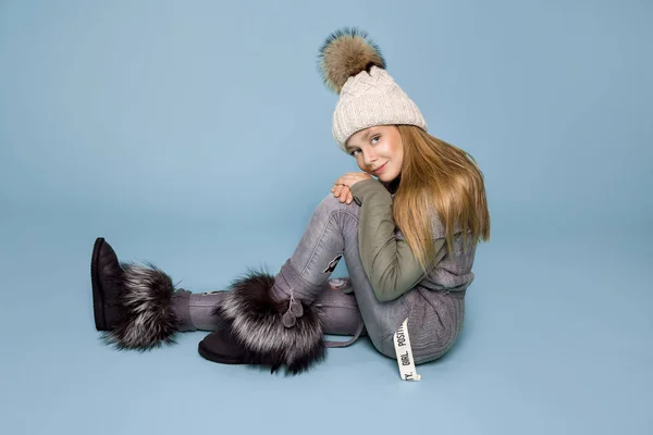 Söt liten flicka klädd i vinterkläder, hatt och vinter jacka med päls, stående på blå bakgrund — Stockfoto