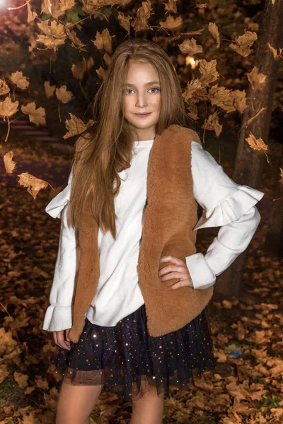 Το χαριτωμένο μικρό κορίτσι ντυμένοι στα παλτό και μπότες κάθεται σε Φθινοπωρινό φόντο, Χρυσή φθινόπωρο φύλλα. — Φωτογραφία Αρχείου