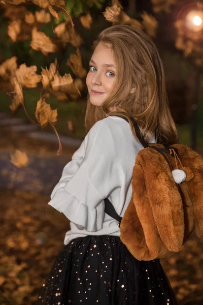 Linda niña vestida con abrigo y botas sentadas sobre fondo de otoño, hojas doradas de otoño . — Foto de Stock
