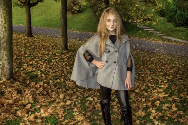 Cute little girl dressed in coat and boots sitting on autumn background, golden autumn leaves. — Stock Photo, Image