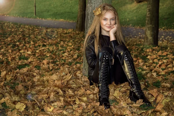 Το χαριτωμένο μικρό κορίτσι ντυμένοι στα παλτό και μπότες κάθεται σε Φθινοπωρινό φόντο, Χρυσή φθινόπωρο φύλλα. — Φωτογραφία Αρχείου