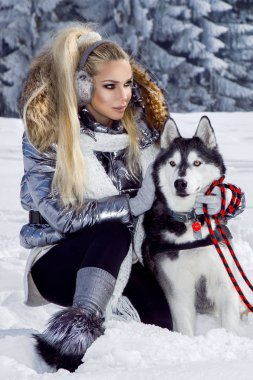 Güzel sarışın kadın, kar üzerinde duran ve Husky köpek tutarak. Arka planda dağlar ve kar güzel bir görünümü vardır.