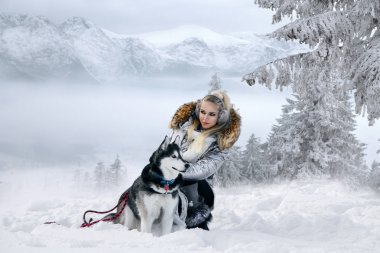 Güzel sarışın kadın, kar üzerinde duran ve Husky köpek tutarak. Arka planda dağlar ve kar güzel bir görünümü vardır.