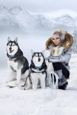Güzel sarışın kadın, kar üzerinde duran ve Husky köpek tutarak. Arka planda dağlar ve kar güzel bir görünümü vardır.