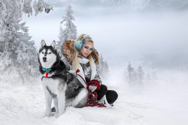Güzel sarışın kadın, kar üzerinde duran ve Husky köpek tutarak. Arka planda dağlar ve kar güzel bir görünümü vardır.