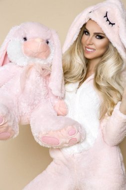 Beautiful sexy blonde woman wearing a pajama, a bunny costume, smiling happily. Fashion model on a beige background in  Easter bunny costume. clipart