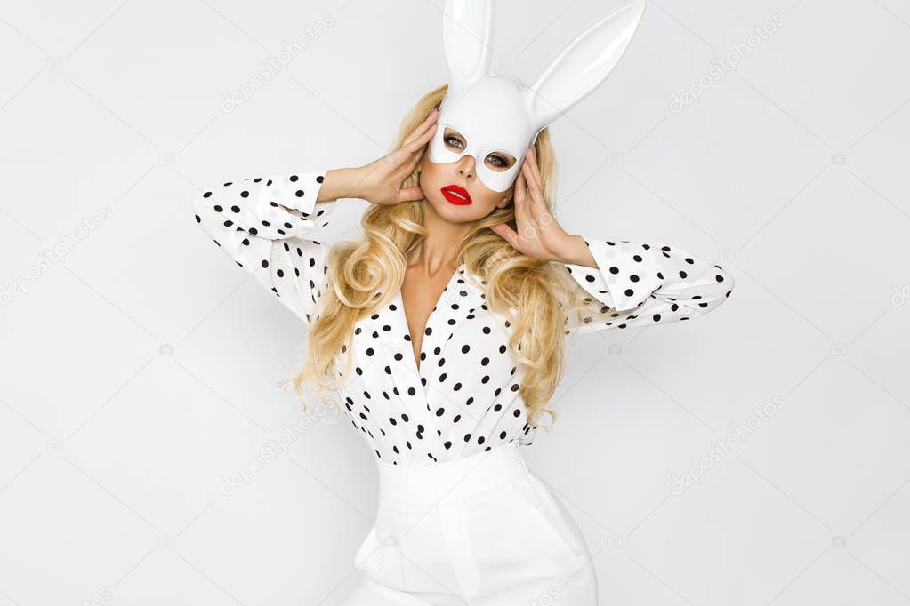 Beautiful, sexy blonde woman in elegant clothes in polka dots and in a white rabbit mask
