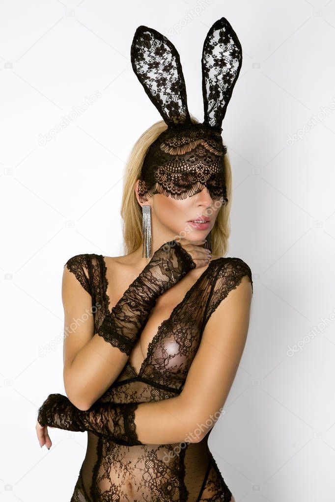 Beautiful, sexy blonde woman in elegant lingerie and black lace Easter bunny mask, standing on white background