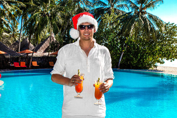 Christmas Santa Claus on the pool at the ocean. Christmas Maldives beach. Santa Clause hat male model in the Maldives holds drinks. Happy New Year travel space for hot countries concept - image