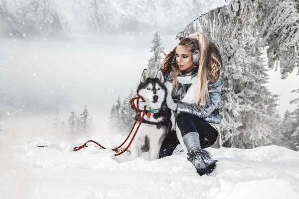 Hermosa mujer rubia, de pie sobre la nieve y sosteniendo perros Husky . — Foto de Stock
