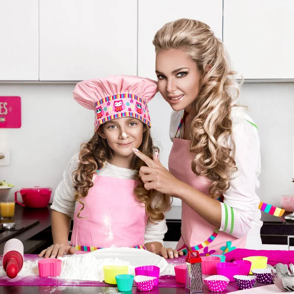 Beautiful funny girl daughter kid in aprons kitchen cooking in the kitchen  cookies and pasta noodles and cakes Stock Photo by ©marcink3333 169353722