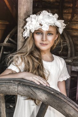 Küçük güzel bir kızın portresi. Çelenkli ve beyaz elbiseli güzel bir kızın moda portresi. Bahar modası ve komünyon konsepti.