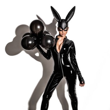 Lateks kostüm ve siyah tavşan maskesi içinde poz veren ve balonları beyaz arka planda tutan seksi sarışın güzel kadın. Paskalya tavşanı kavramı.