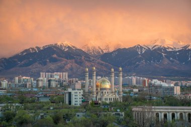 Almaty, Kazakistan - Nisan 2020: Yeşil şehirde, dağların önünde altın kubbeli modern cami. Almaty 'de günbatımı. Pencereden en iyi görünüm.