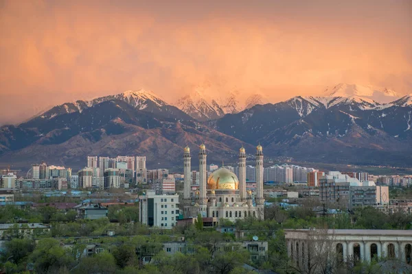 Almaty, Kazakistan - Nisan 2020: Yeşil şehirde, dağların önünde altın kubbeli modern cami. Almaty 'de günbatımı. Pencereden en iyi görünüm.