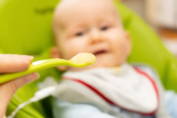 Colher cheia de mingau de cereal e bebê desfocado feliz no fundo. Foco seletivo na colher. Bebê primeiro soilds. Desmame . — Fotografia de Stock