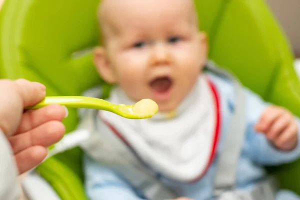 Colher cheia de mingau de cereal e bebê desfocado feliz no fundo. Foco seletivo na colher. Bebê primeiro soilds. Desmame . — Fotografia de Stock