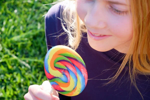 Jovem loira feliz segura pirulito arco-íris em um pau — Fotografia de Stock