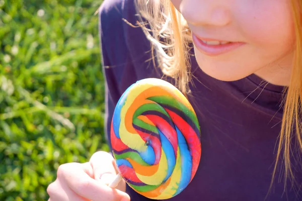 Jovem loira feliz segura pirulito arco-íris em um pau — Fotografia de Stock