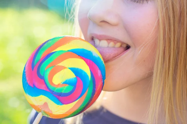 Happy blonde young girl holds rainbow lollipop on a stick — Stock Photo, Image