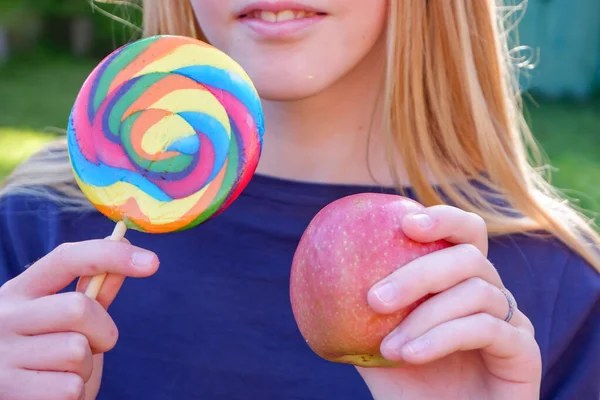 Подростковая блондинка в голубом топе выбирает между нездоровым яблоком и леденцом. Здоровая концепция чистого детоксикации . — стоковое фото