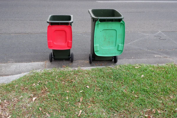 Australian garbage wheelie bins with colourful lids for recycling household waste and green garden waste lined up on the street kerbside for council rubbish collection