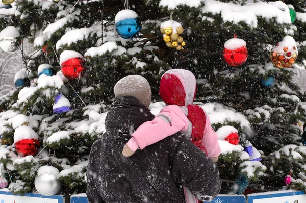 Momentos de Natal: pai e filha vestindo roupas quentes olhando em uma árvore de Natal durante a neve de inverno — Fotografia de Stock