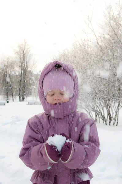 Inverno no parque. Uma menina usando roupas quentes segurando neve na mão e desfrutando de neve no parque — Fotografia de Stock