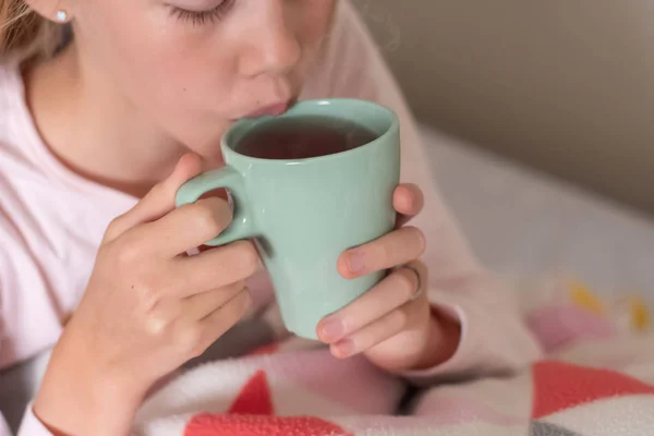 Sick teenage girl sitting on the bed covered with blanket drinking hot tea. Herbal medicine — Stock Photo, Image