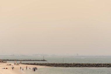 Sydney, Avustralya. 2019-12-21 Avustralya çalı ateşi: Çalı yangınlarından çıkan duman gökyüzünü kaplıyor. İnsanlar Botanik Körfezi sahilinde sıcak hava dalgasından kaçınmaya çalışıyor. Şehir sislerin arasından zar zor görünüyor..