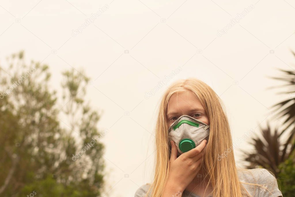 Australian bushfire: blond girl wearing P2 N95 protection respiratory mask to reduce amount of breathing PM2.5 particles from bushfire smoke.