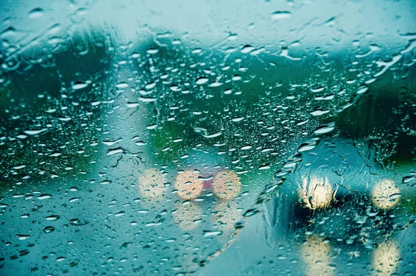 Проливной дождь проливает лобовое стекло. Машины с фарами едва видны на дороге. Селективный фокус — стоковое фото