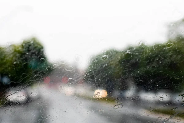 Проливной дождь через лобовое стекло. Машины с фарами едва видны на дороге. Селективный фокус — стоковое фото