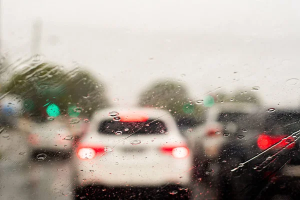 Проливной дождь через лобовое стекло. Машины стоят в очереди на оживленной дороге. Селективный фокус — стоковое фото