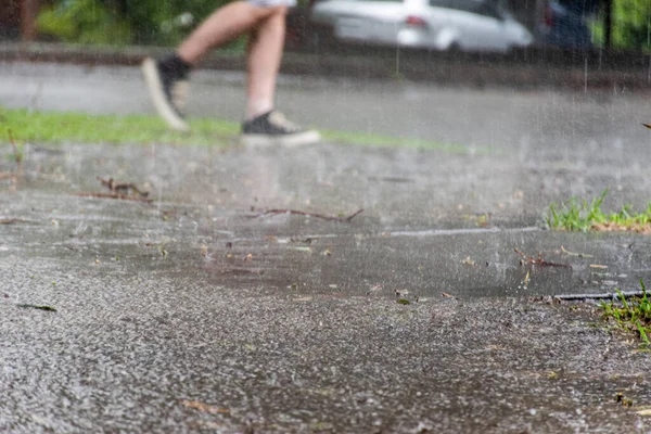 Heavy torrential rain hits the street. Legs are walking along the road