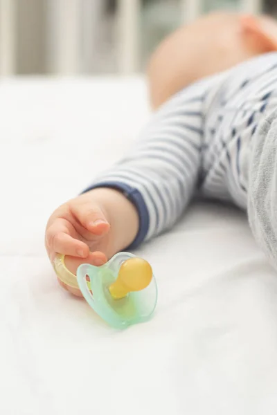 Blureed image of little baby boy who is peacefully sleeping and holding a pacifier dummy in his hand. Selective focus on a dummy — Stock Photo, Image