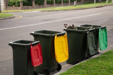 Geri dönüşüm için renkli kapaklı Avustralya çöp kutuları ve belediye çöpleri için kaldırım kenarına dizilmiş genel ev atıkları