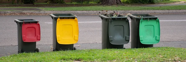 Australian garbage wheelie bins with colourful lids for recycling and general household waste lined up on the street kerbside for council rubbish collection