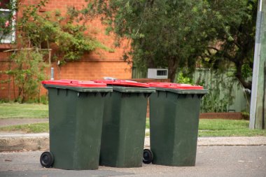 Genel ev atıkları için kırmızı kapaklı Avustralya çöp kutuları konsey çöpleri için kaldırım kenarına dizilmişti..