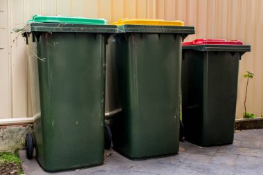 Genel olarak kırmızı ve sarı kapaklı Avustralyalı çöp kutuları ve ev atıklarının geri dönüşümü ve yeniden inşa edilen çitlerinin yakınındaki bahçe atıkları için yeşil kapaklar