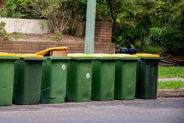Konsey çöplerini toplamak için kaldırım kenarına dizilmiş sarı kapaklı Avustralya çöp kutuları..