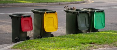 Australian garbage wheelie bins with colourful lids for recycling and general household waste lined up on the street kerbside for council rubbish collection clipart