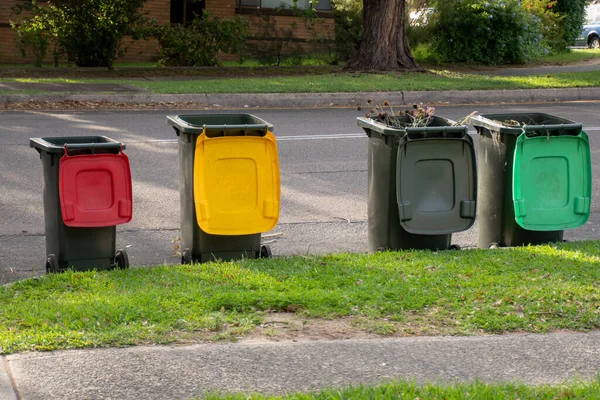 Australian garbage wheelie bins with colourful lids for recycling and general household waste lined up on the street kerbside for council rubbish collection