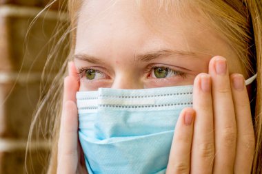 Virüslerin yayılmasını önlemek için tek kullanımlık yüz maskesi takan bir kız. Coronavirus ve COVID-19 Konsepti